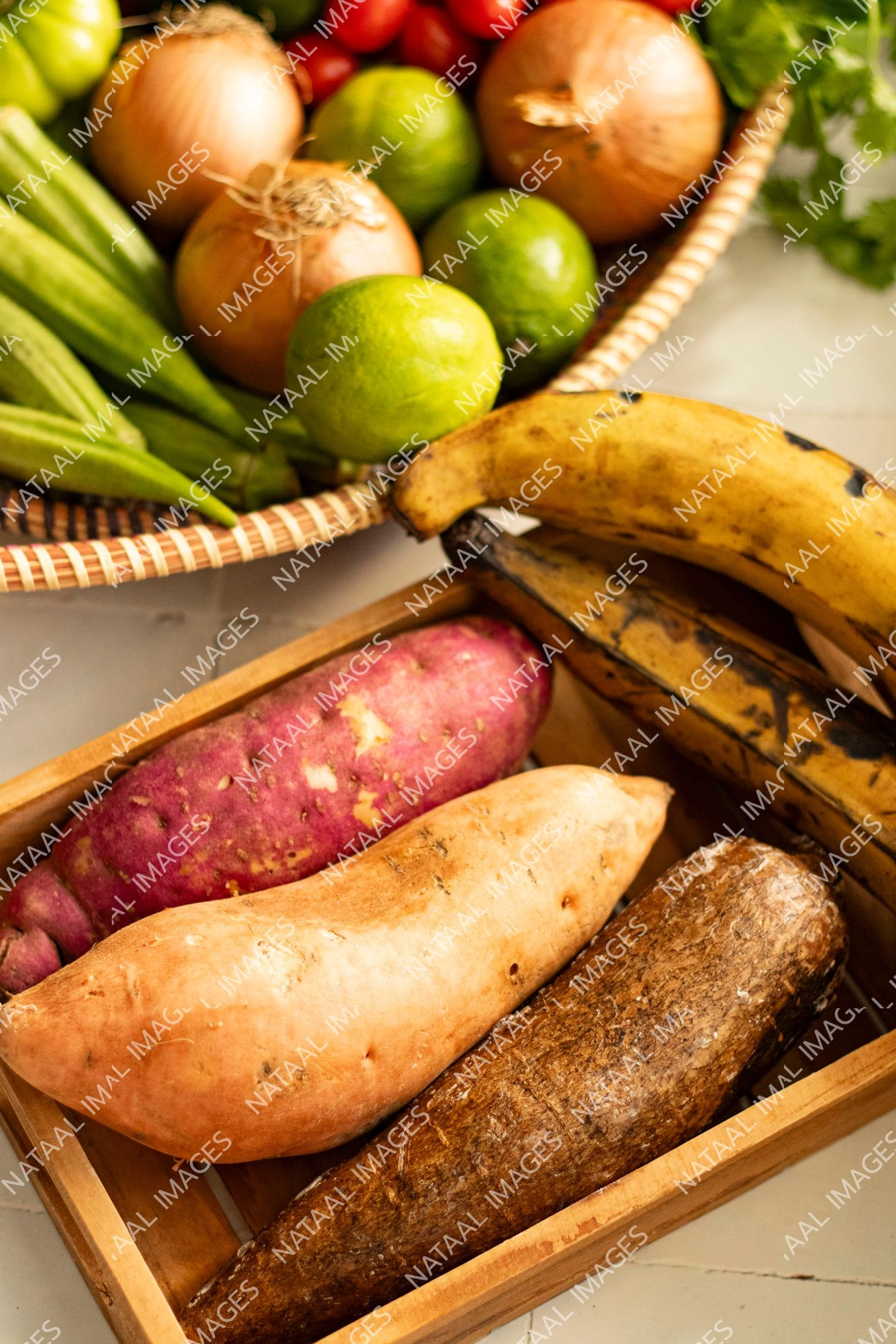 bananes plantains ignames et patates douces dans un plateau en bois sur un plan de travail carrele