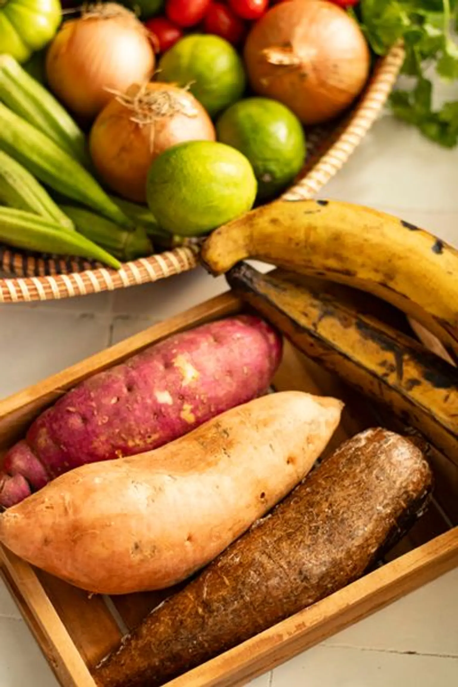 bananes plantains ignames et patates douces dans un plateau en bois sur un plan de travail carrele
